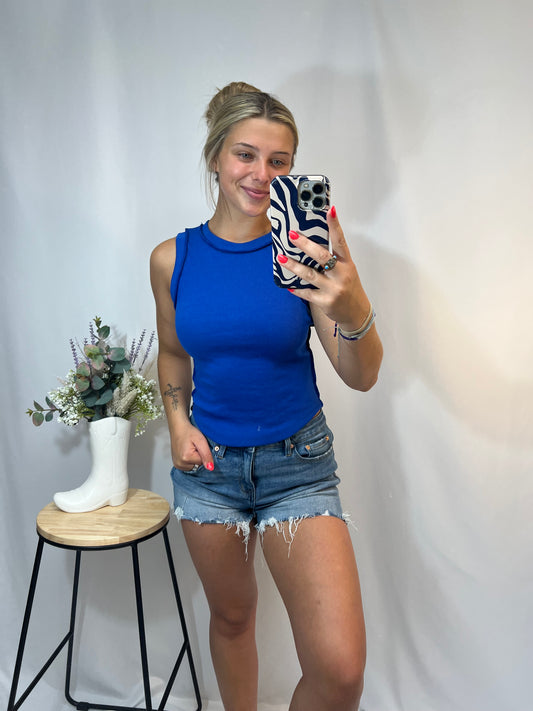 Young woman in royal blue ribbed high neck fitted tank top, styled with denim shorts – trendy summer tank for girls.