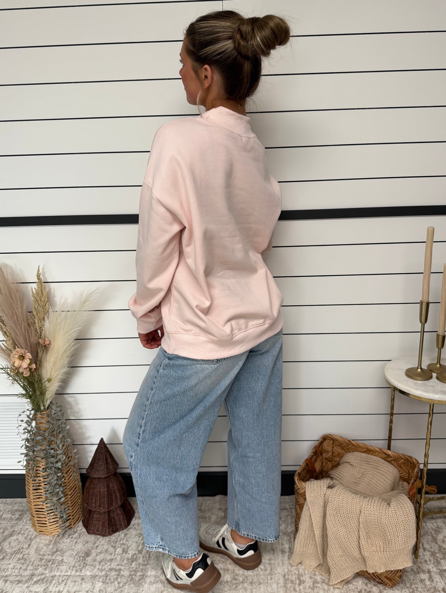 Person wearing a pink hoodie and blue jeans standing on a wooden floor.