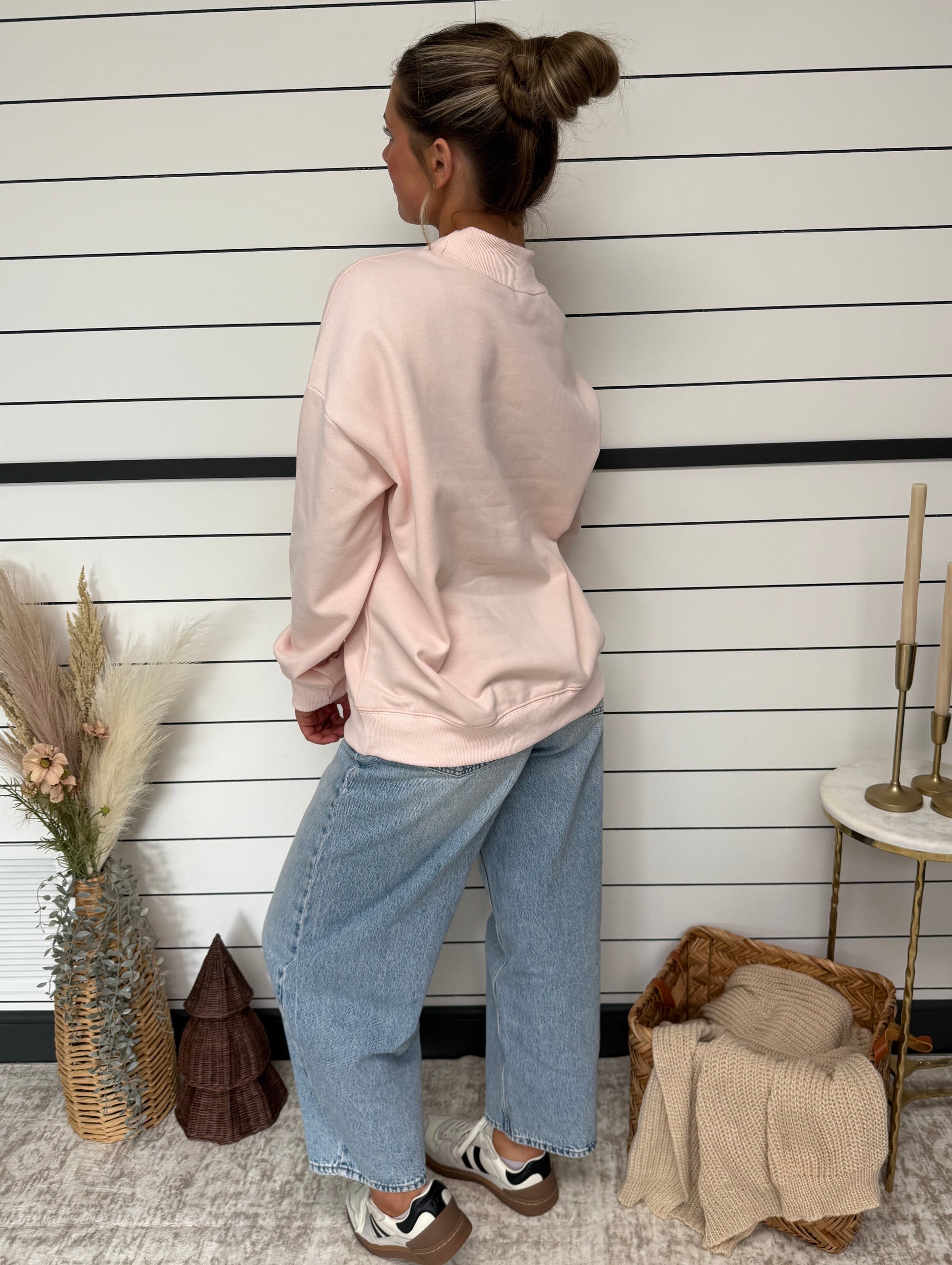 Person wearing a pink hoodie and blue jeans standing on a wooden floor.