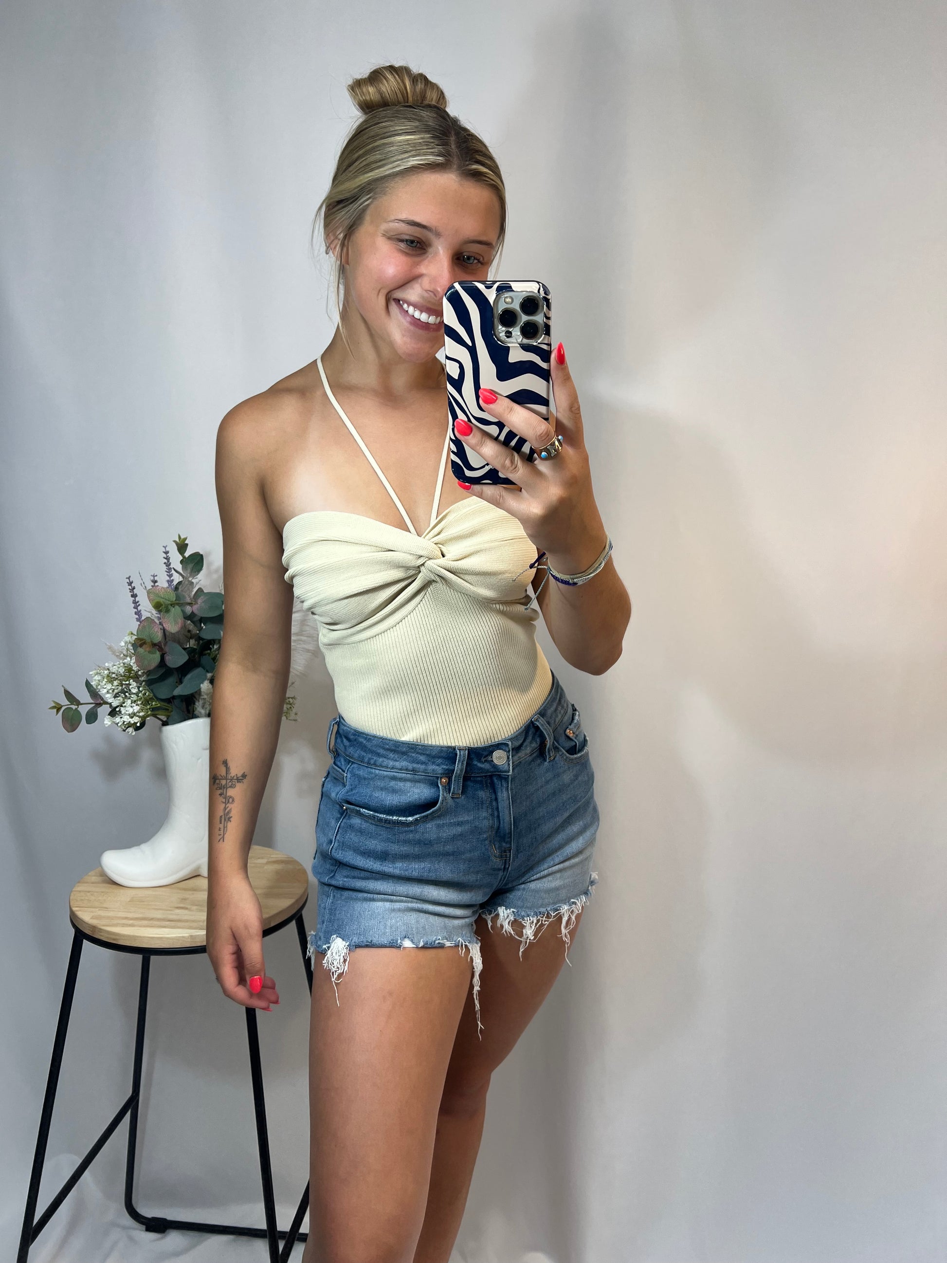 Woman wearing cream knit ruched halter top with high-rise denim shorts