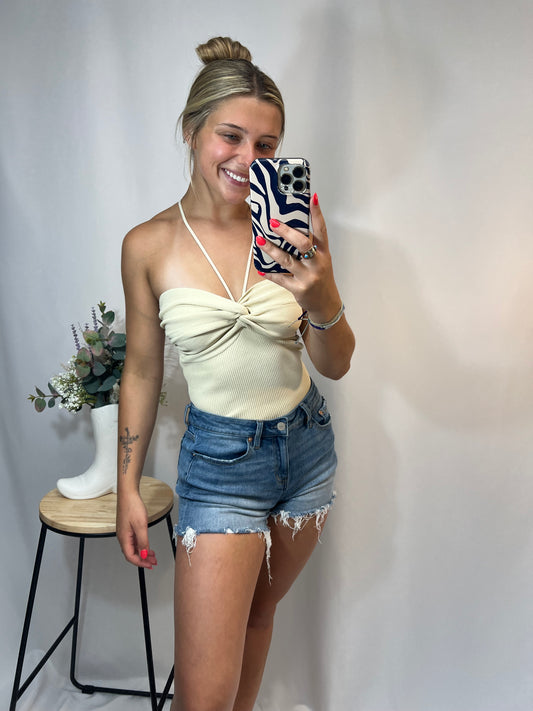 Woman wearing cream knit ruched halter top with high-rise denim shorts