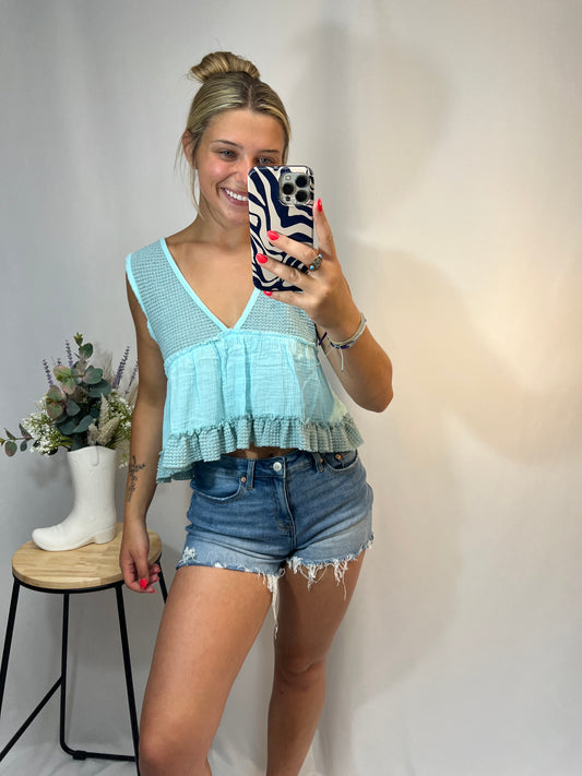 Woman wearing baby blue cropped babydoll tank top with denim shorts
