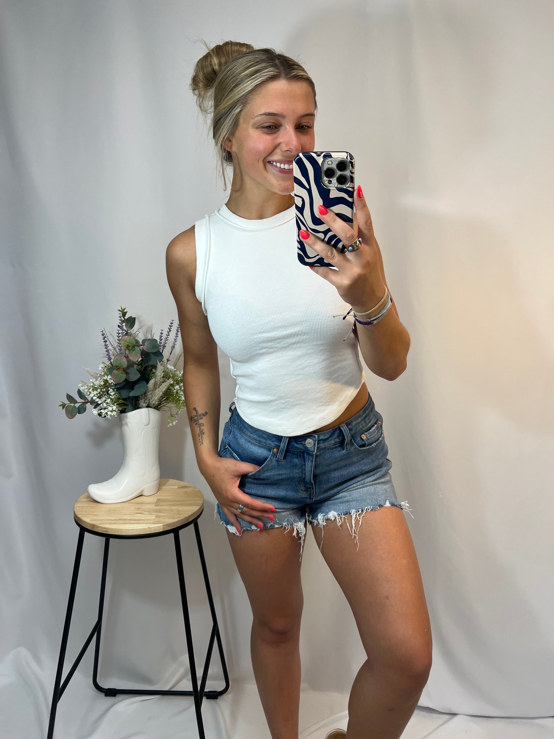Girl wearing a white ribbed high neck tank top with exposed seam detail styled with denim shorts – cute summer basics for young women.