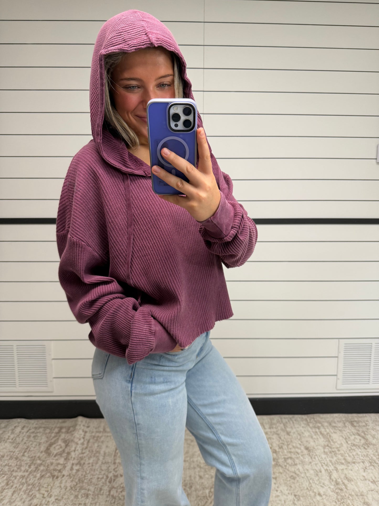 Person wearing a purple hoodie and light blue jeans taking a selfie with a phone.