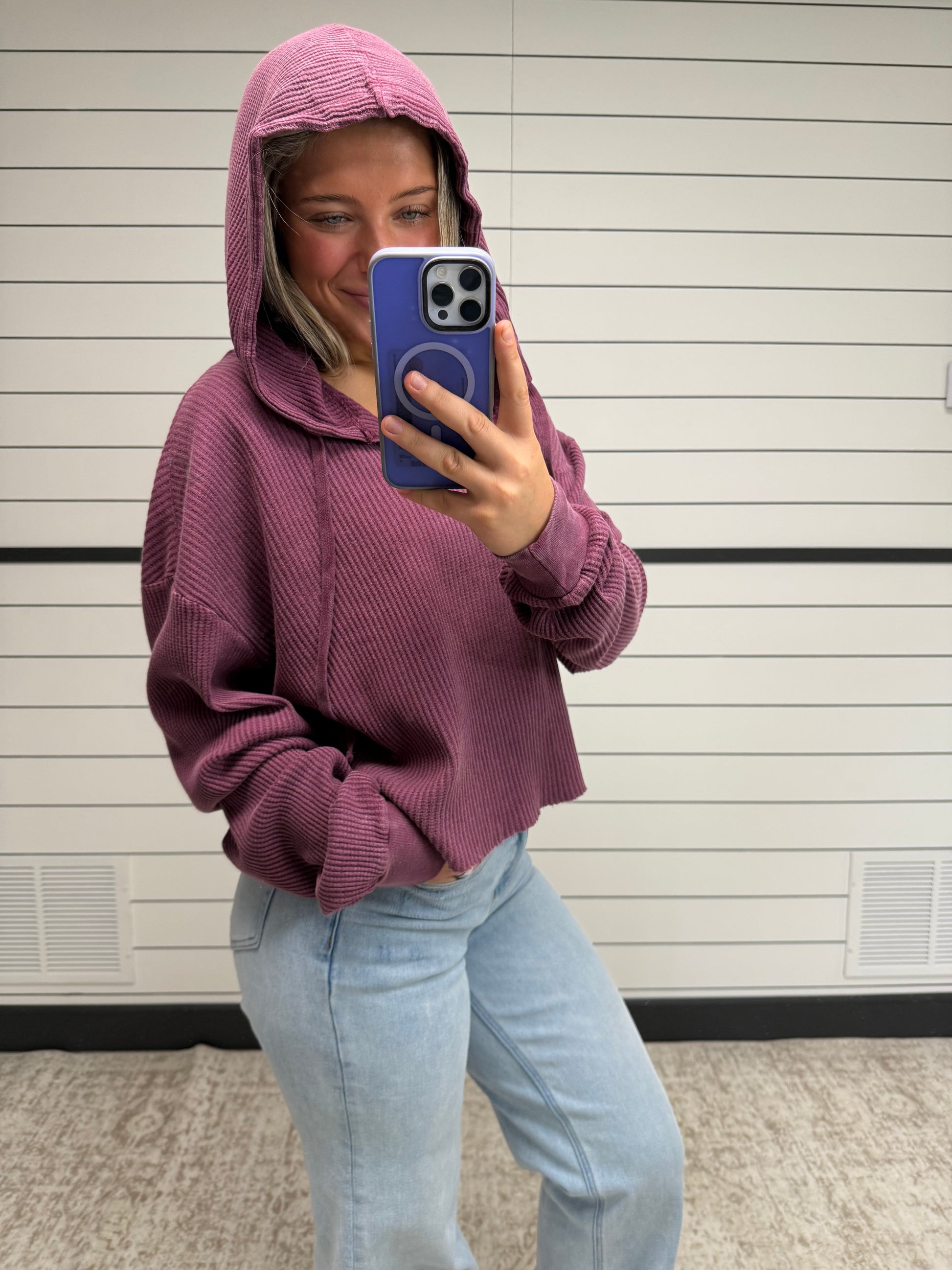 Person wearing a purple hoodie and light blue jeans taking a selfie with a phone.