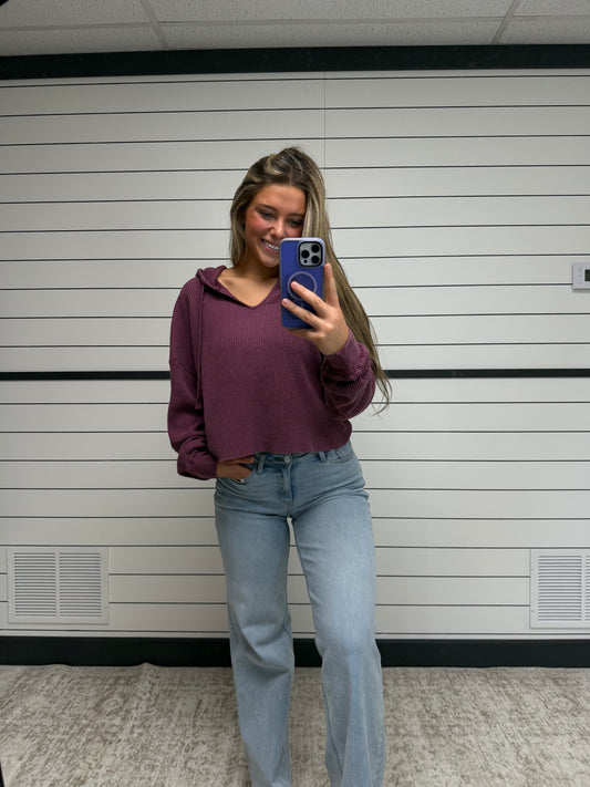 Person taking a mirror selfie wearing a purple hoodie and blue jeans in a bathroom.