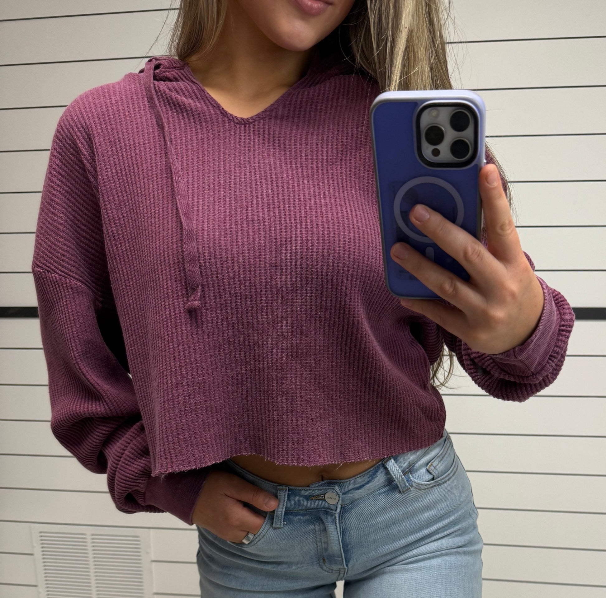 Person wearing a purple sweater and light blue jeans, taking a photo with a phone.