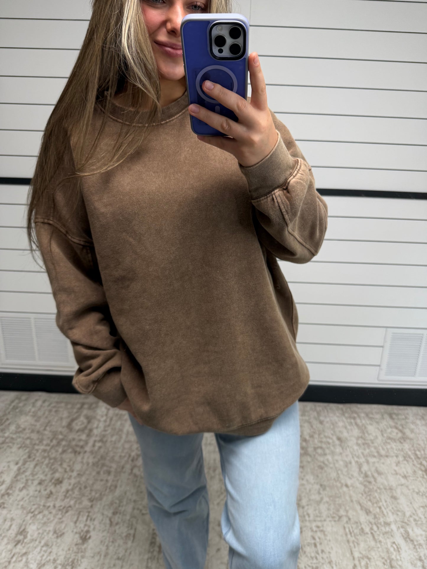 Person wearing a brown sweatshirt taking a mirror selfie.