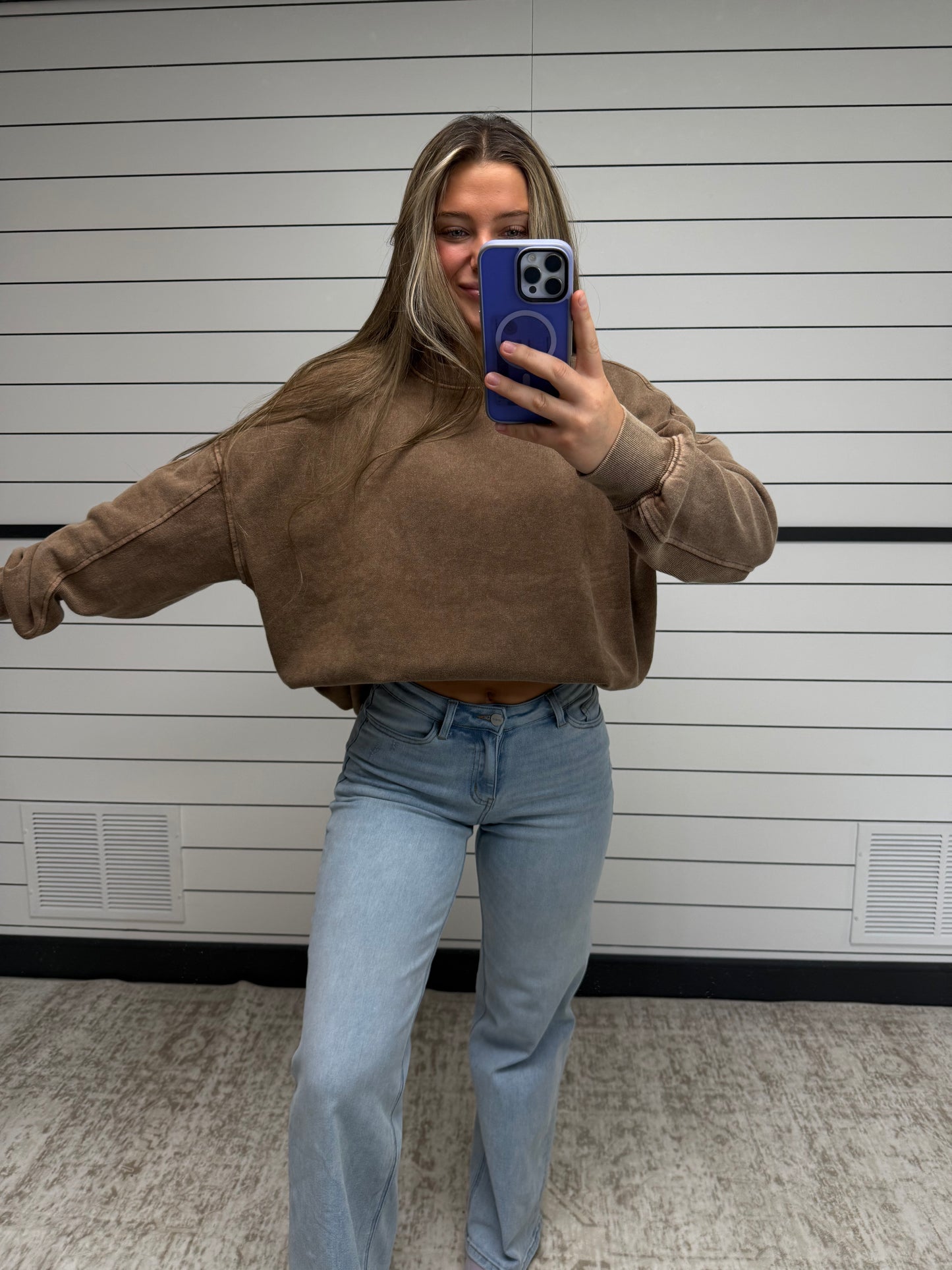 Person wearing a brown hoodie and blue jeans taking a mirror selfie.