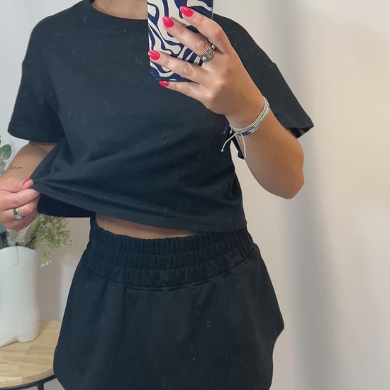 Woman modeling black cropped t-shirt and matching ruffle skort set
