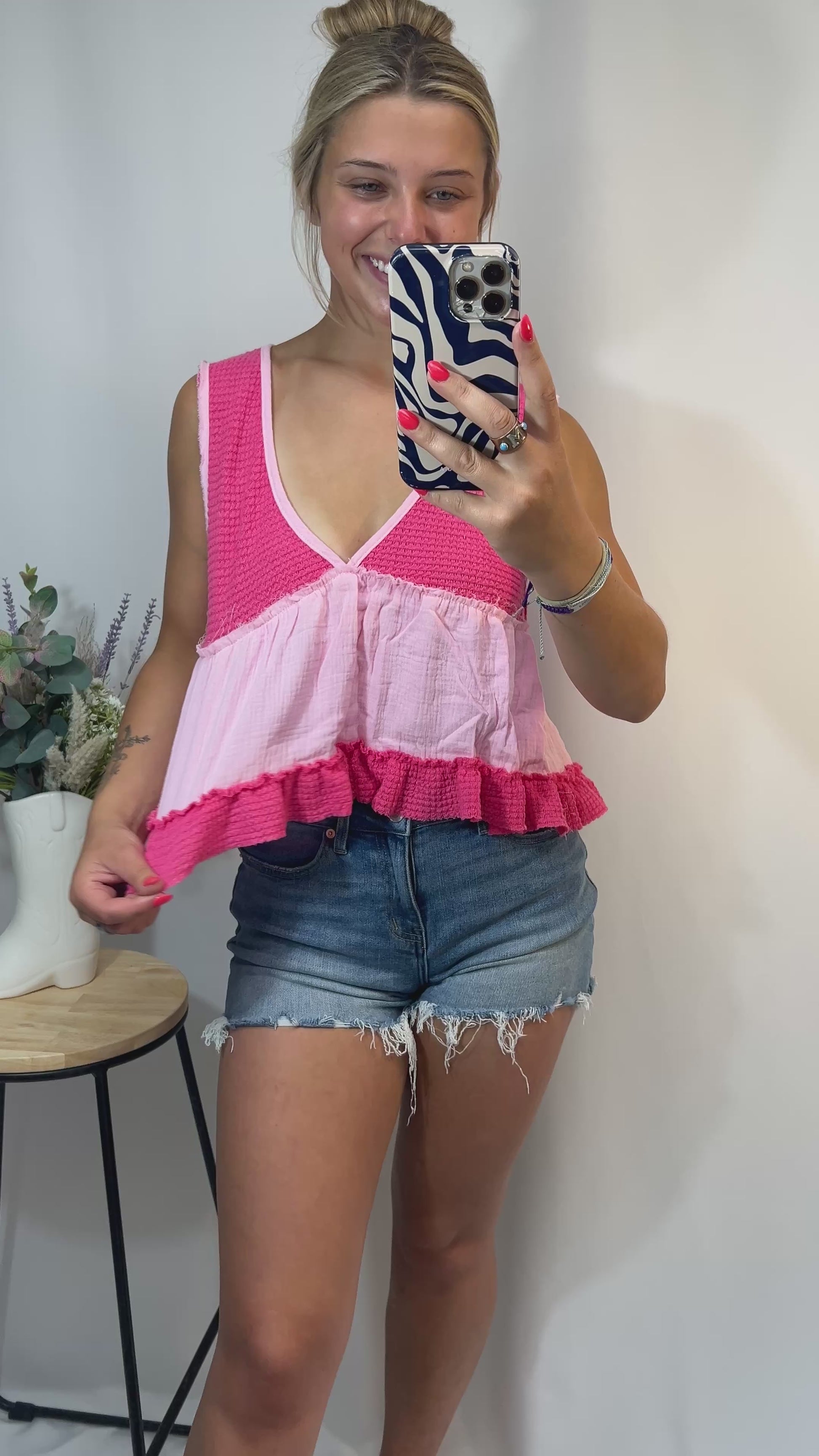 Playful styling of pink babydoll tank top paired with denim shorts, model smiling and posing