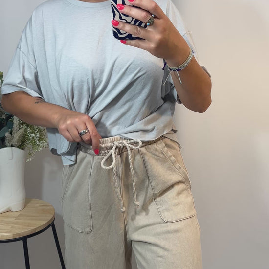 Model showing front and side of beige wide leg lounge pants with adjustable drawstring waist and raw hem for trimming