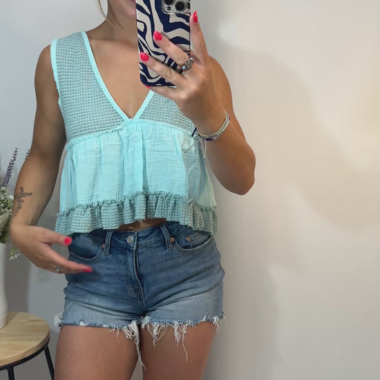 Model twirling in mint cropped babydoll tank with ruffle hem and denim shorts