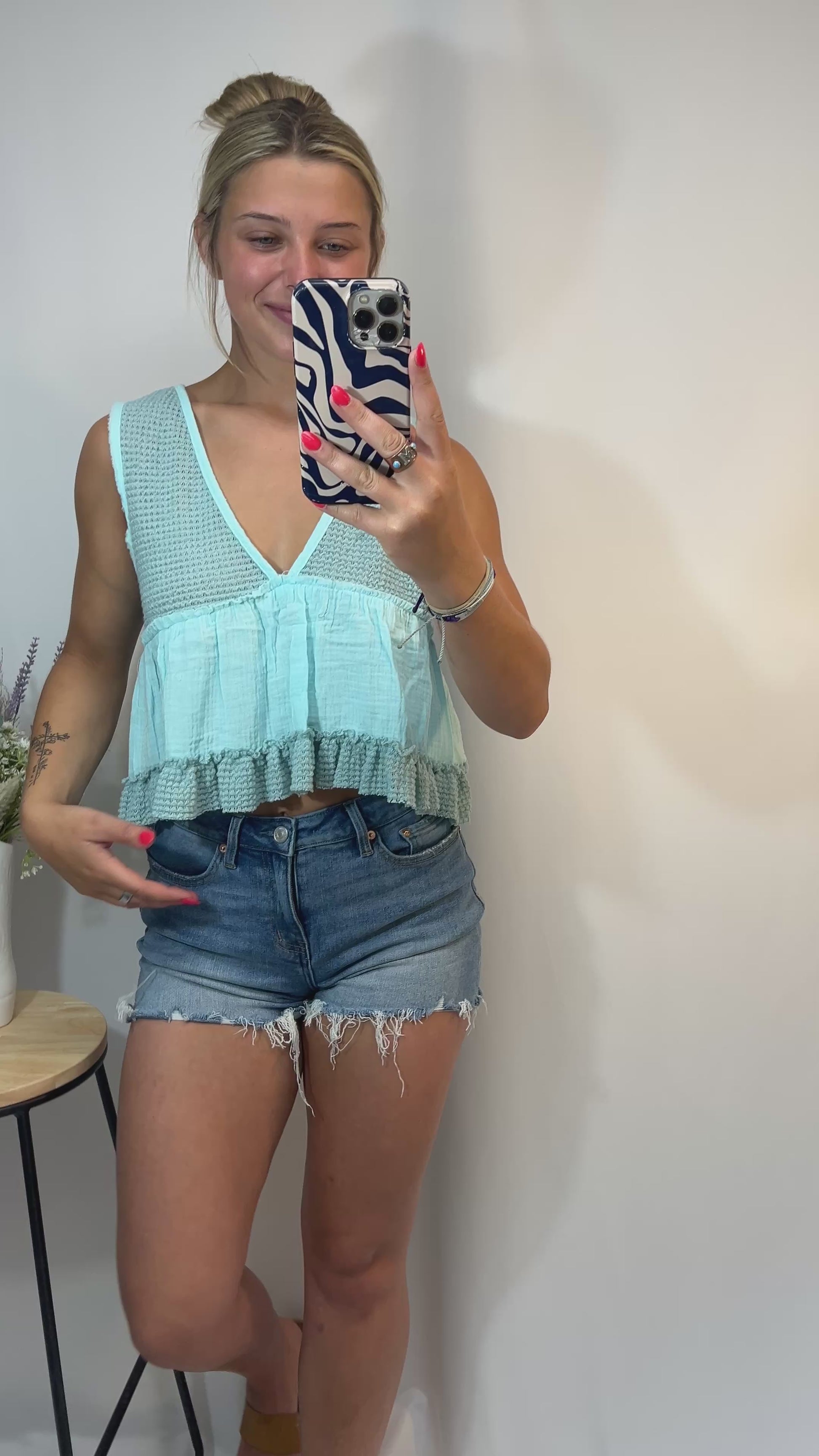 Model twirling in mint cropped babydoll tank with ruffle hem and denim shorts