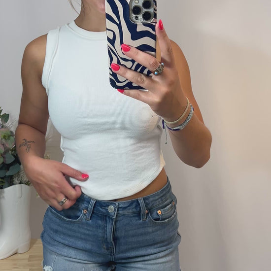 360 view of girl modeling white ribbed cotton tank top with high neckline and raw hem, styled for casual streetwear or layering.
